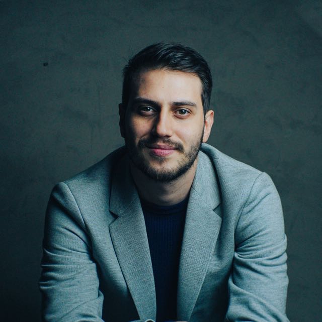 Homem com terno cinza e barba olhando para frente.